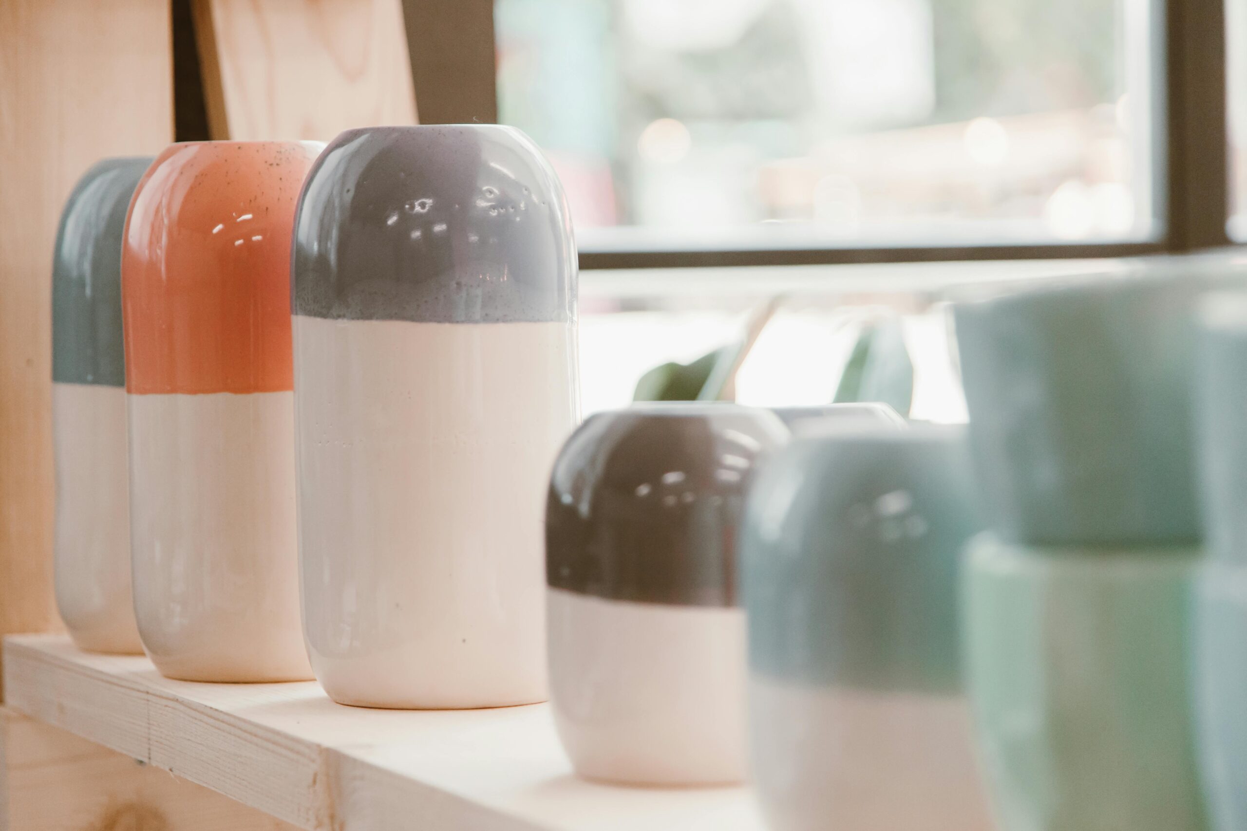 Aesthetic ceramic vases in various colors displayed on a wooden shelf indoors.